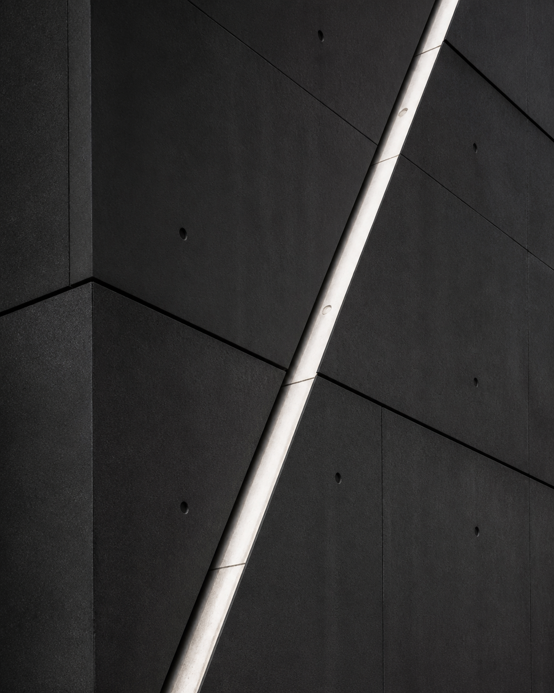 Dark charcoal concrete facade divided by a diagonal pale channel